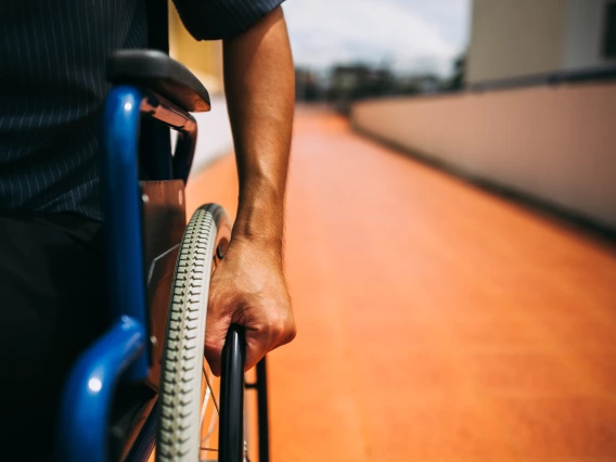 Person in a wheel chair with their hand holding the wheel.